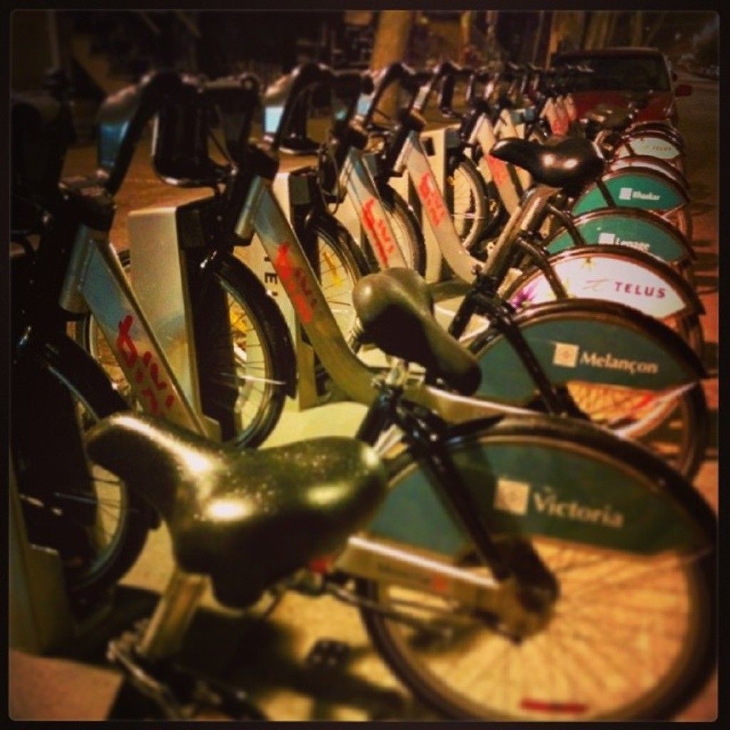 In the middle of the image we can see some bicycles. Behind the bicycles there is a vehicle.