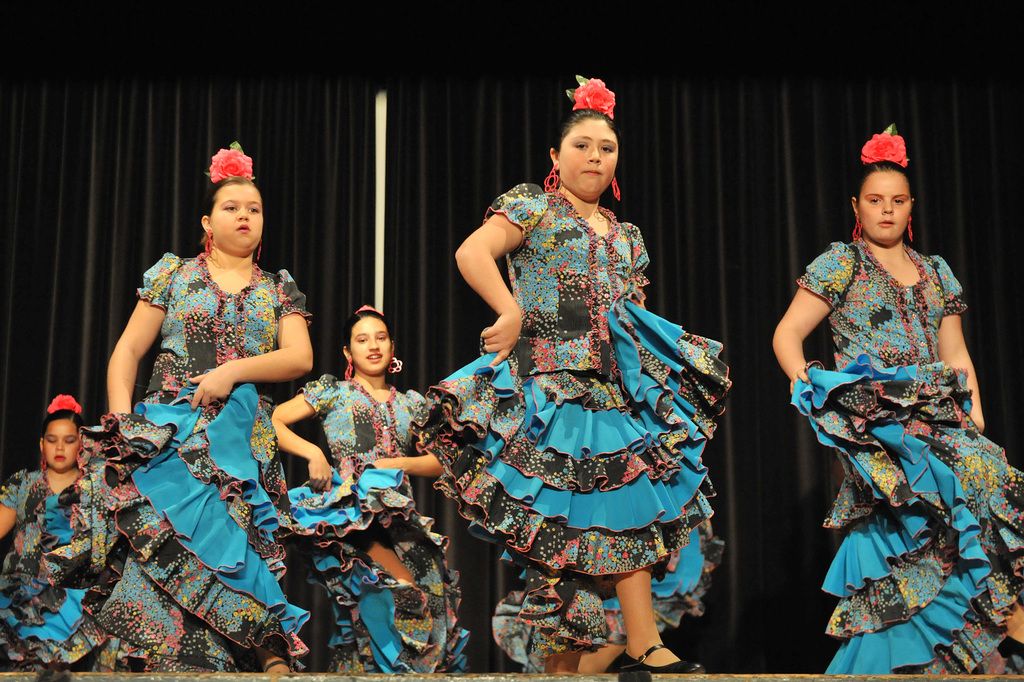This picture shows few women dancing on the dais and we see black color cloth on the back. All the...