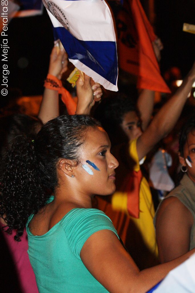 In this picture we can see the women wearing green t-shirt standing in the protest and holding the...