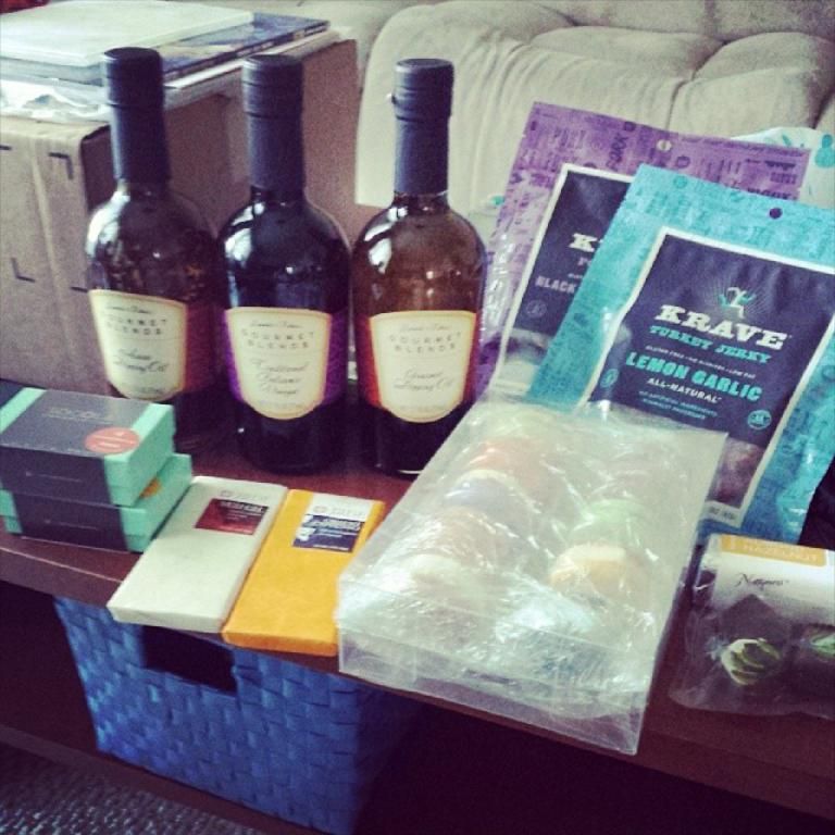 In the image there are few wine bottles on the table,beside them there are some food items wrapped...