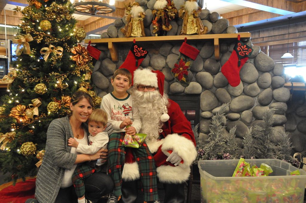 There is a lady, children and a man in santa claus dress. Man is wearing specs and gloves. Boy is...