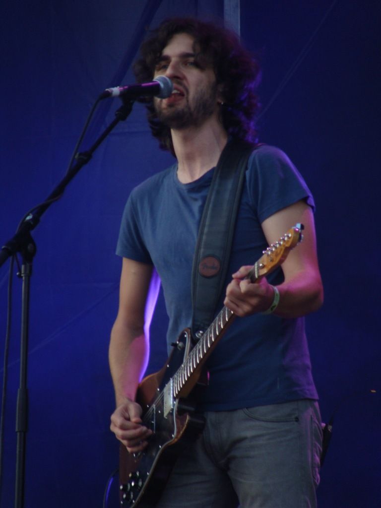 a person is standing, playing guitar and singing. in front of him there is a microphone. he is...