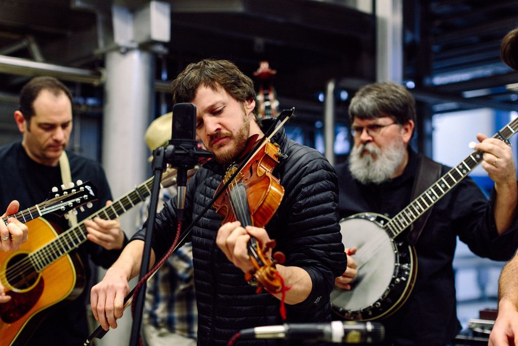 In the picture there are many musicians playing musical instruments. There is a mic in front of the...