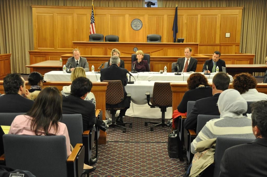 This is a meeting hall where we can see a group of people sitting on chairs and also two flags of...