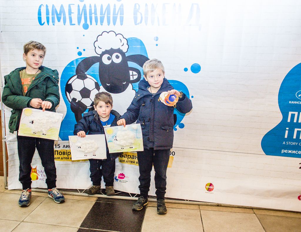 In the middle of the image three children are standing and holding some papers. Behind them there...