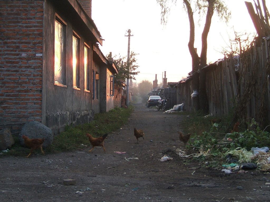 In this picture, there is a lane in the center. Towards the left, there are buildings and poles....