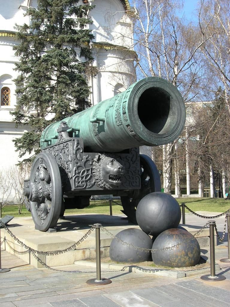 In this image we can see tsar cannon, behind this there is a building and trees.