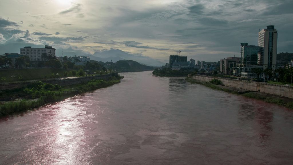 In this image there is a big river beside that there are so many buildings and plants.