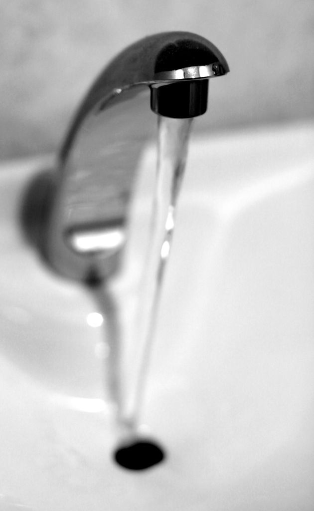 This is a black and white image, in this image there is a tap and water flowing from the tap.