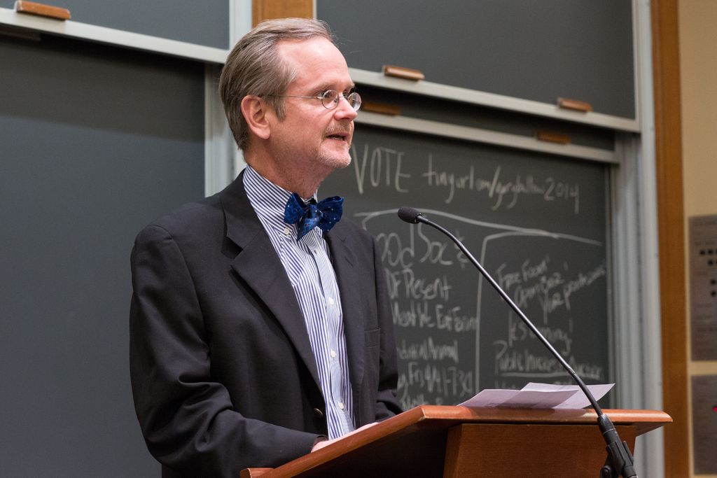 This image consists of a man wearing a black suit is standing in front of the podium and talking in...