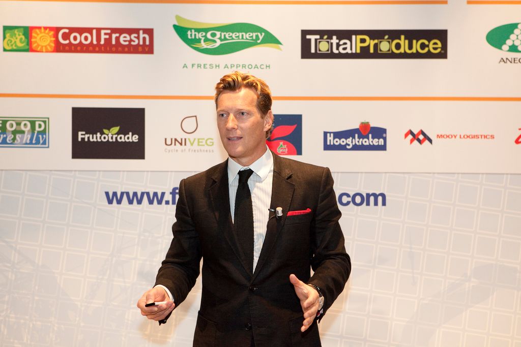 In this picture, we see the man in the black blazer is standing. He is holding something in his...