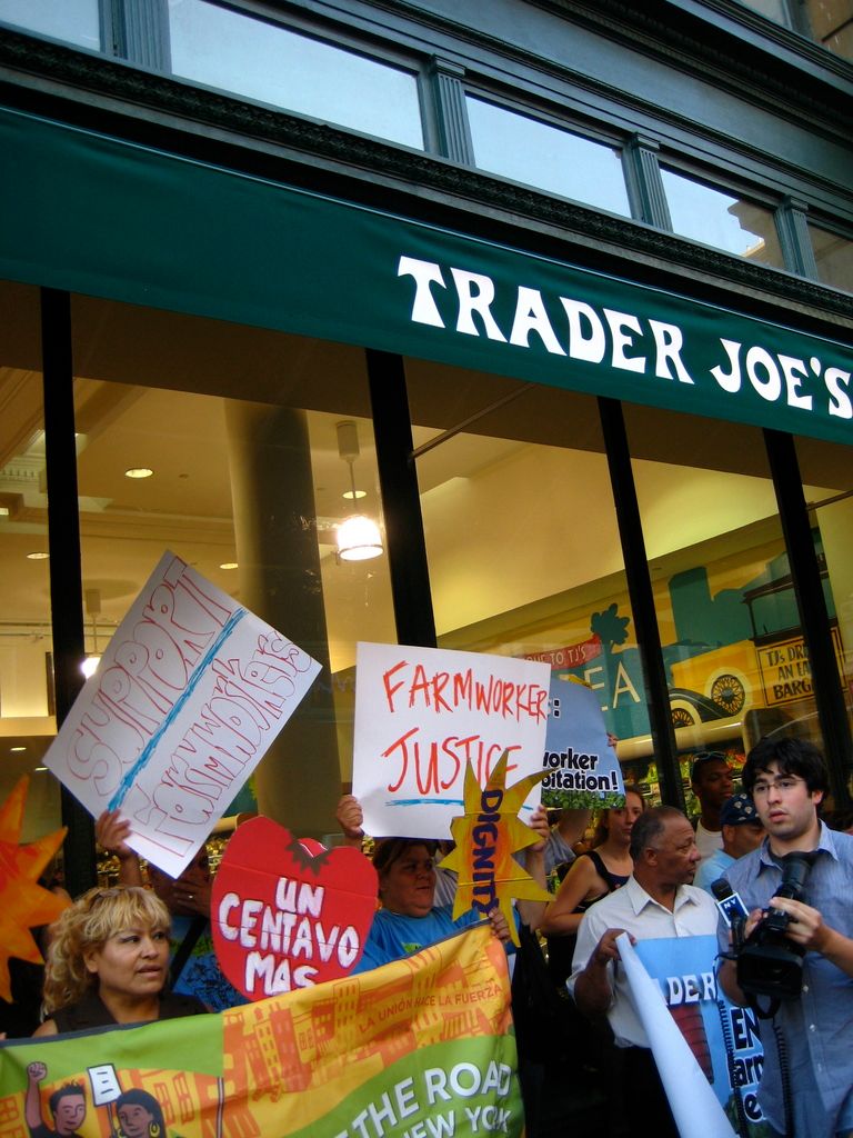 Here in this picture we can see a group of people standing near a store and protesting with banners...