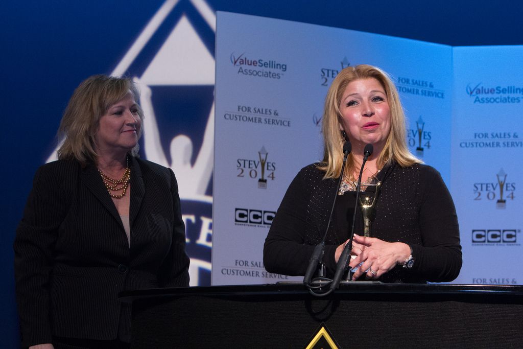 This picture is clicked inside. On the left there is a woman smiling and standing. On the right...