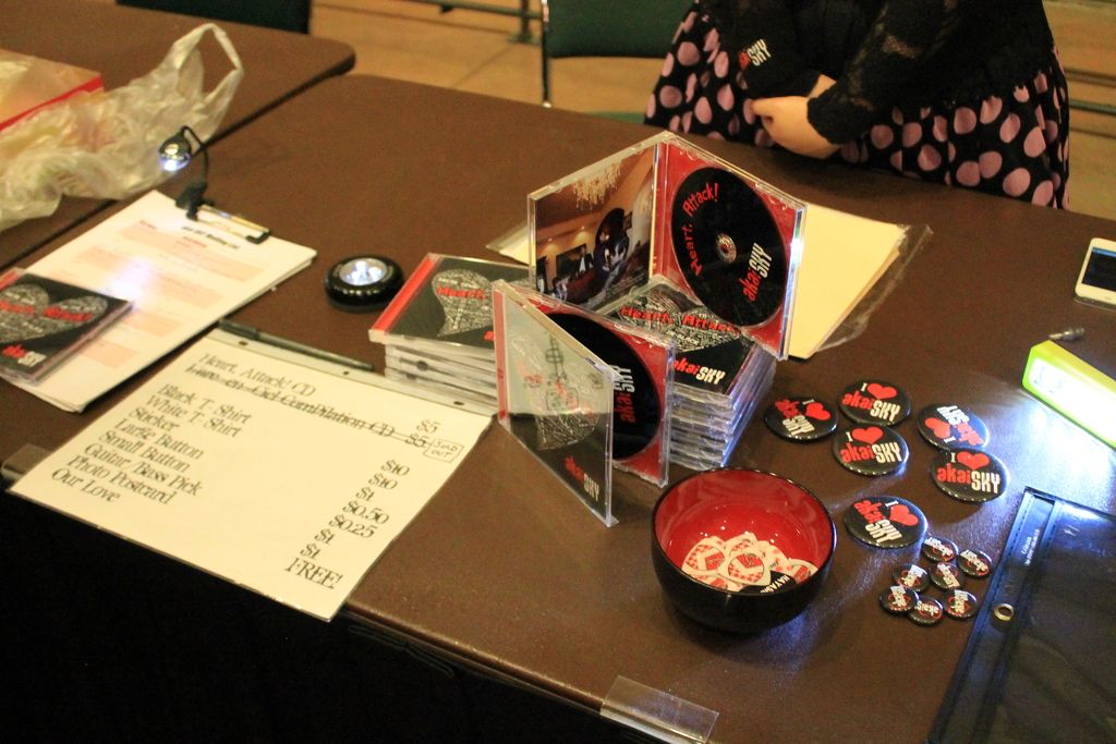 There is a table in which there are CD cases in bundle and badges and a cup with coupons in it. And...