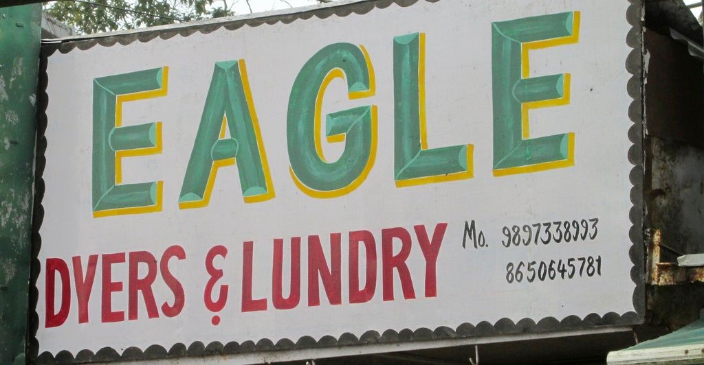 There is a hoarding on which eagle is written. Behind that there is tree and a wire.