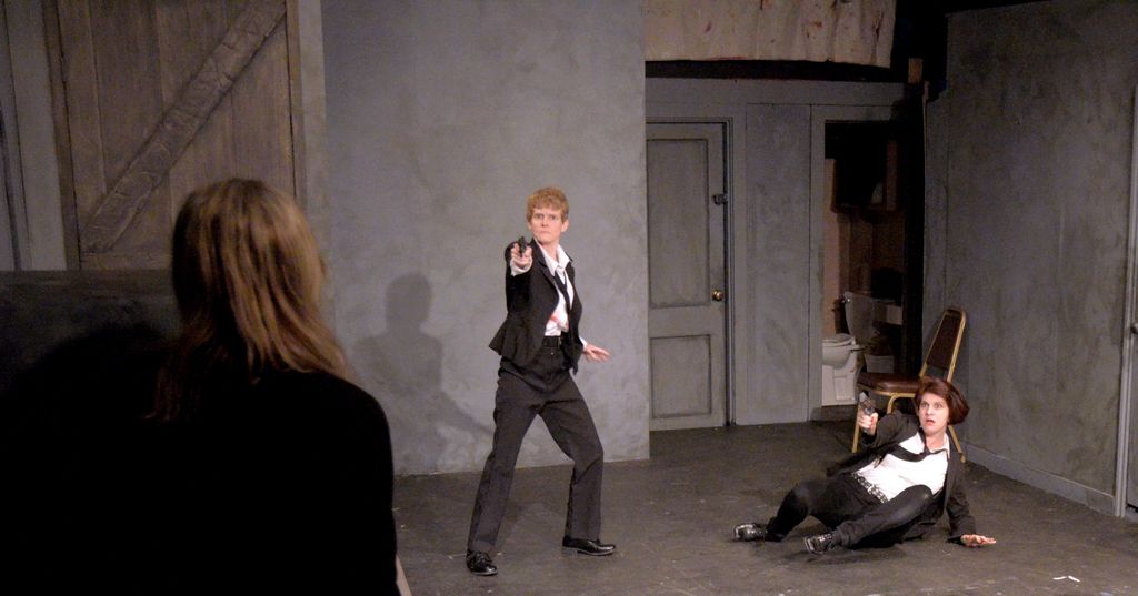 This picture shows an interview of a room. We see a woman seated on the ground and holding a gun in...