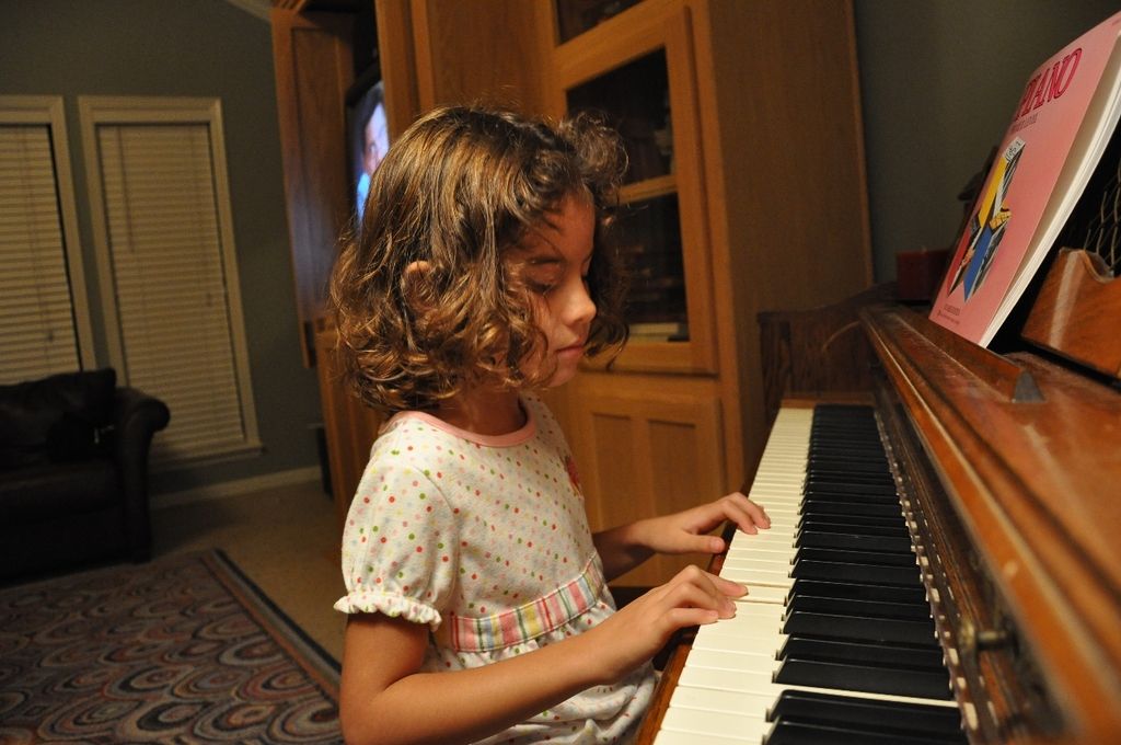 Here we can see a child playing a piano which is present in front of her and there is a book on the...