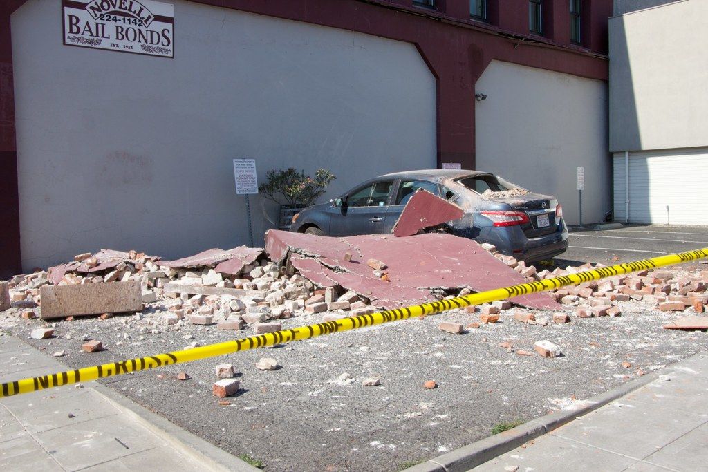 In the image we can see there is a broken wall on the ground and there are red bricks of the wall...