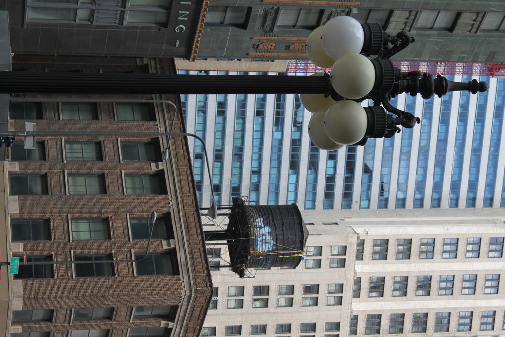 In this image we can see a few buildings, there are some poles, lights and windows, at the top of...