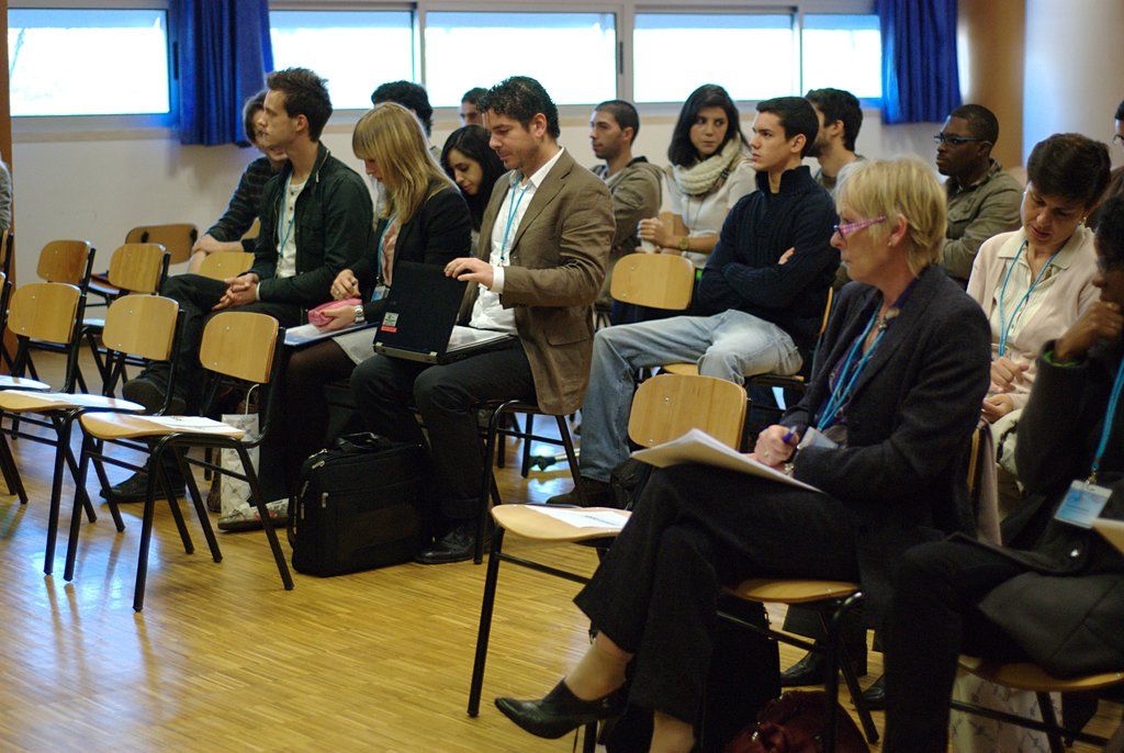 Here we can see few persons sitting on chairs wearing id cards. This is a floor. this is a bag....