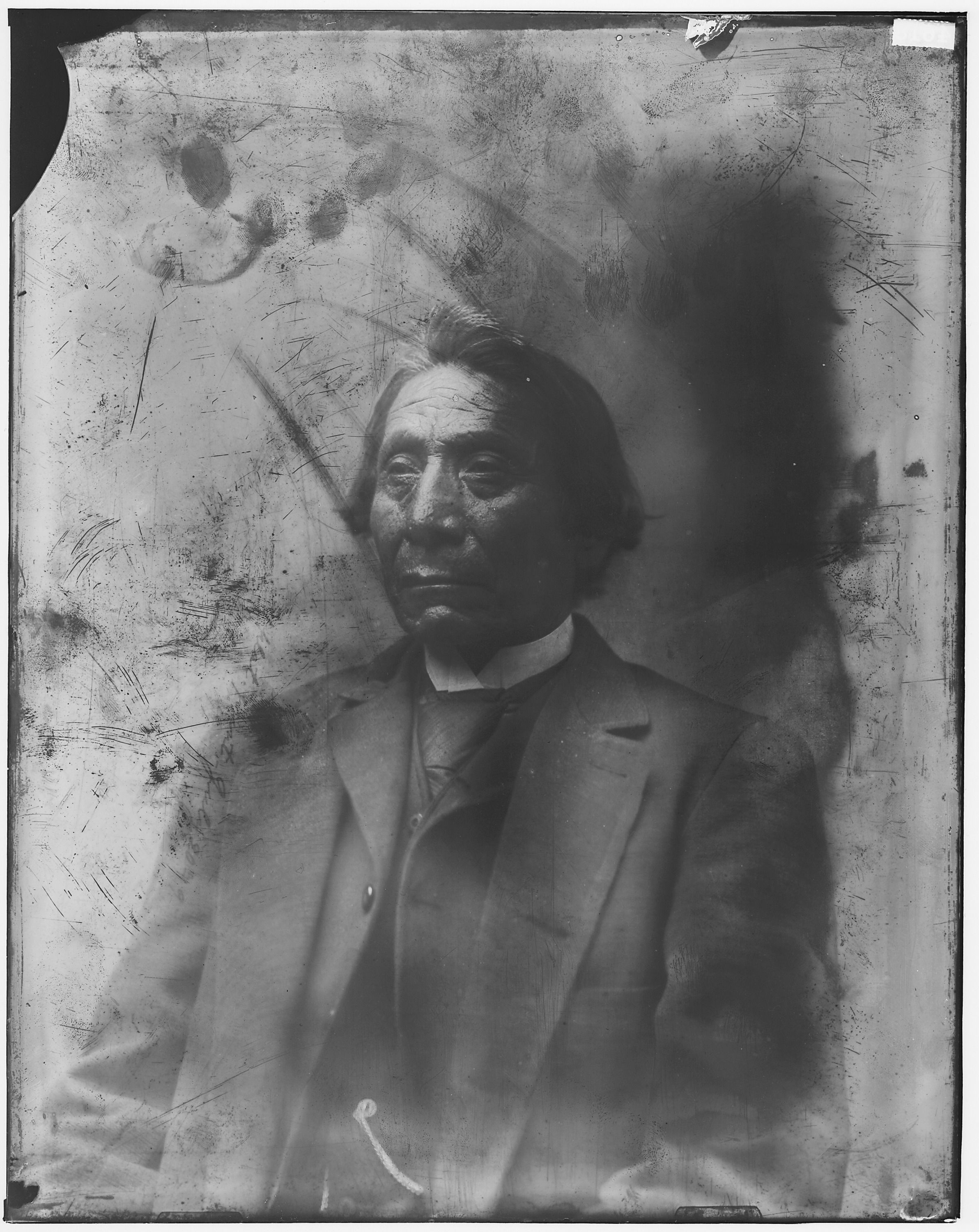 The image shows an old black and white photo of an Indian man wearing a suit. His face is clearly...