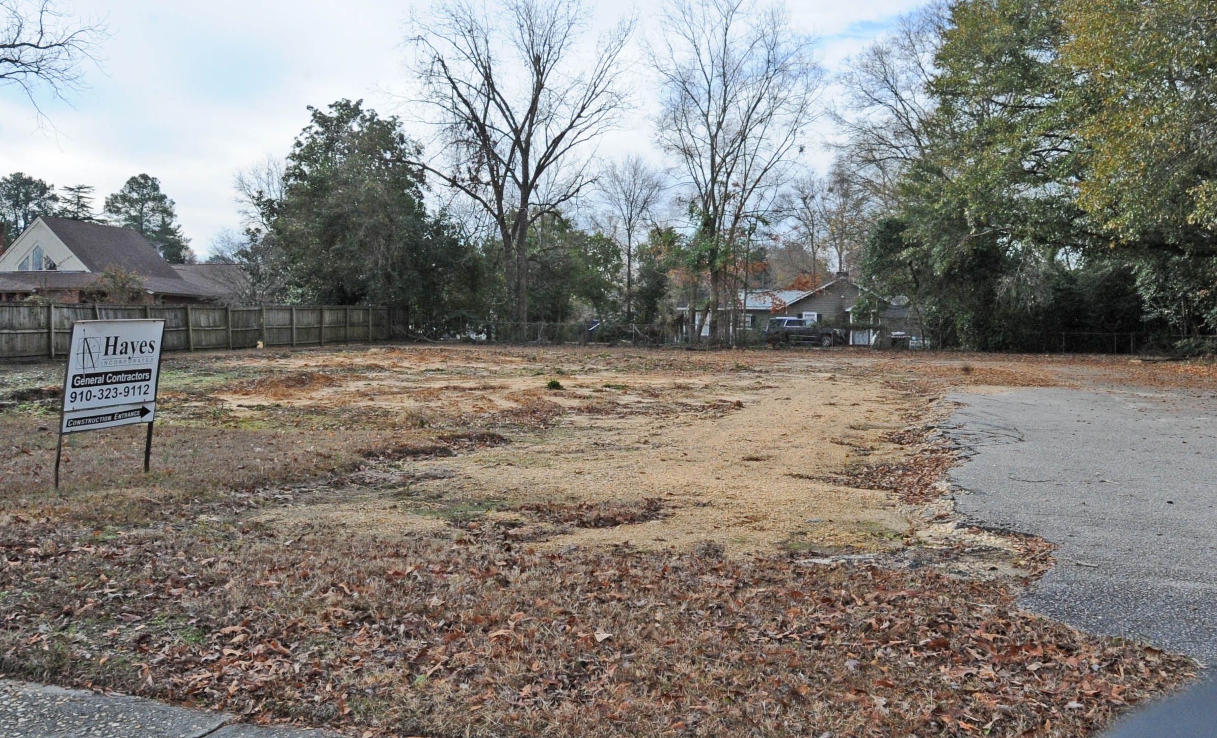 The image shows a vacant lot with a sign in the middle of it, surrounded by dry leaves on the...