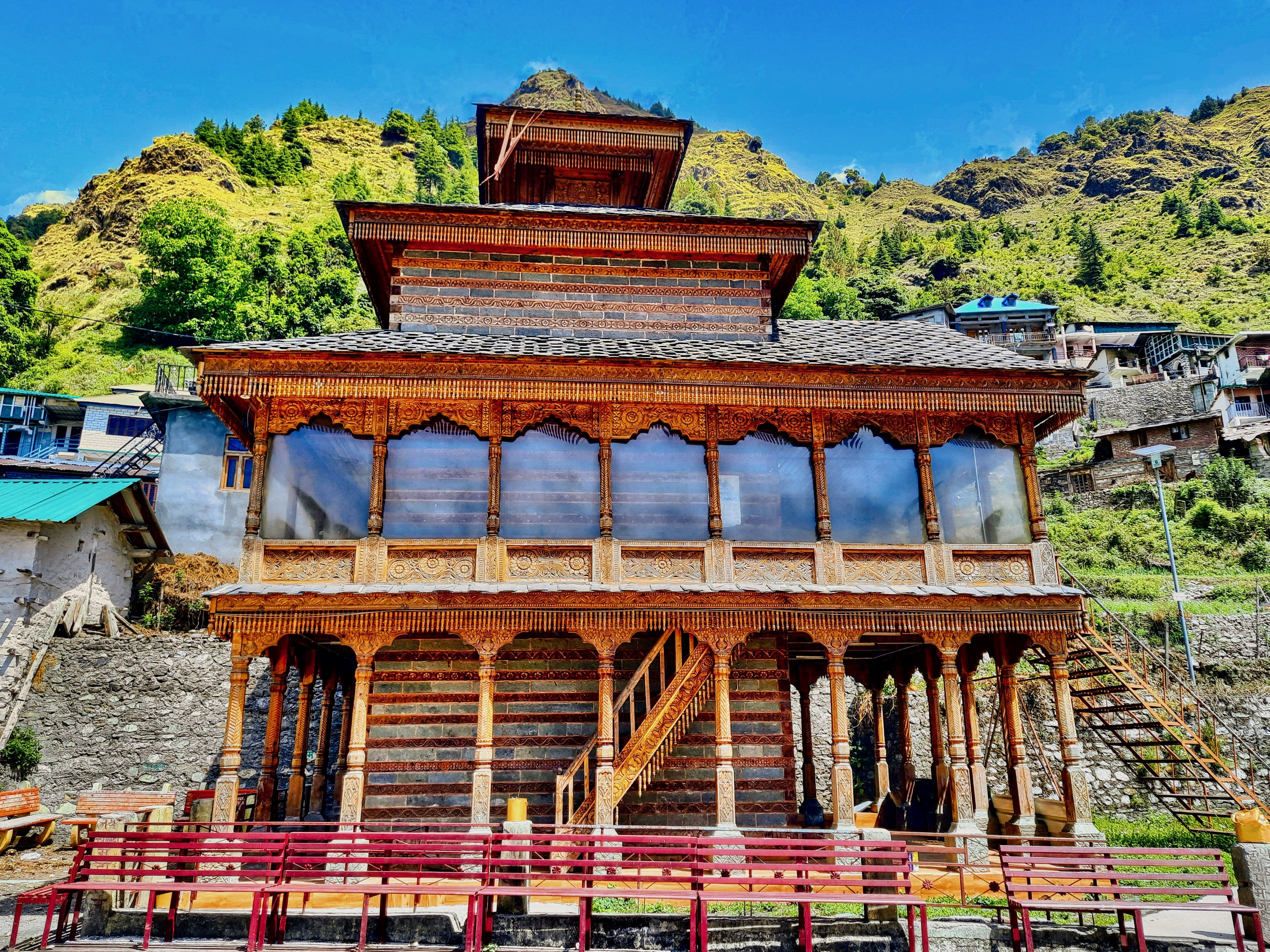 The image shows a large wooden building with a red bench in front of it, surrounded by stairs,...