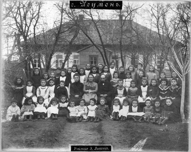 The image shows a black and white photo of a group of children posing for a picture in front of a...