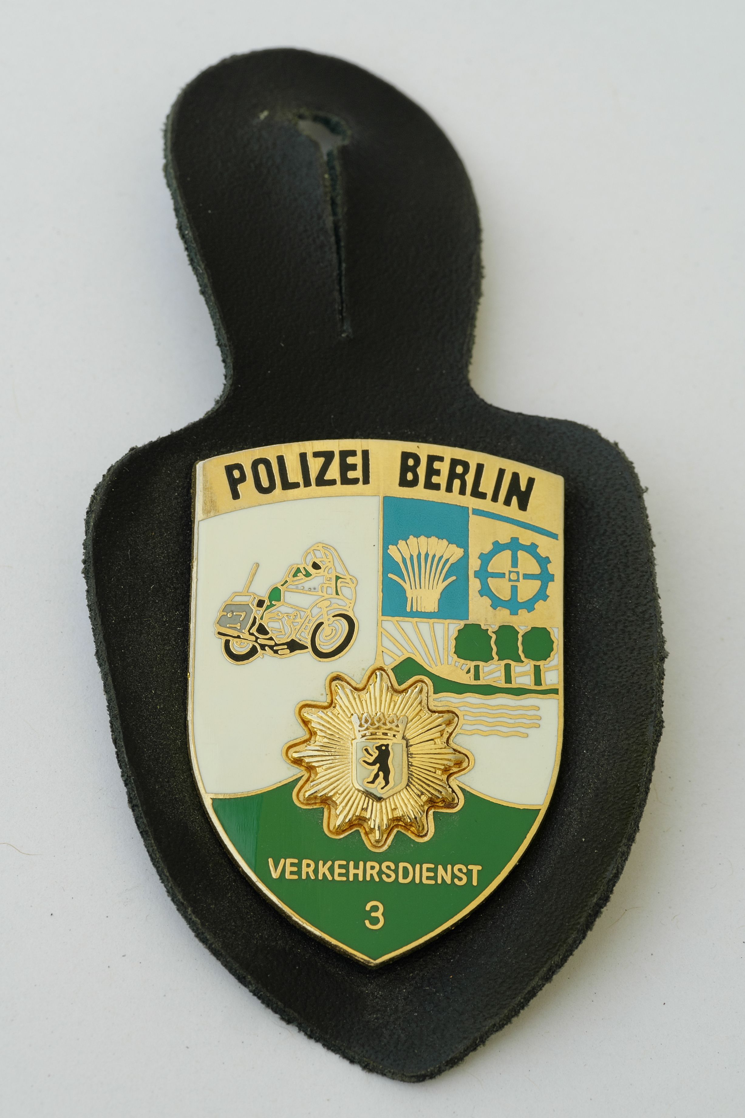 The image shows a police badge with the words "Police Berlin" on it, placed on a surface. The badge...