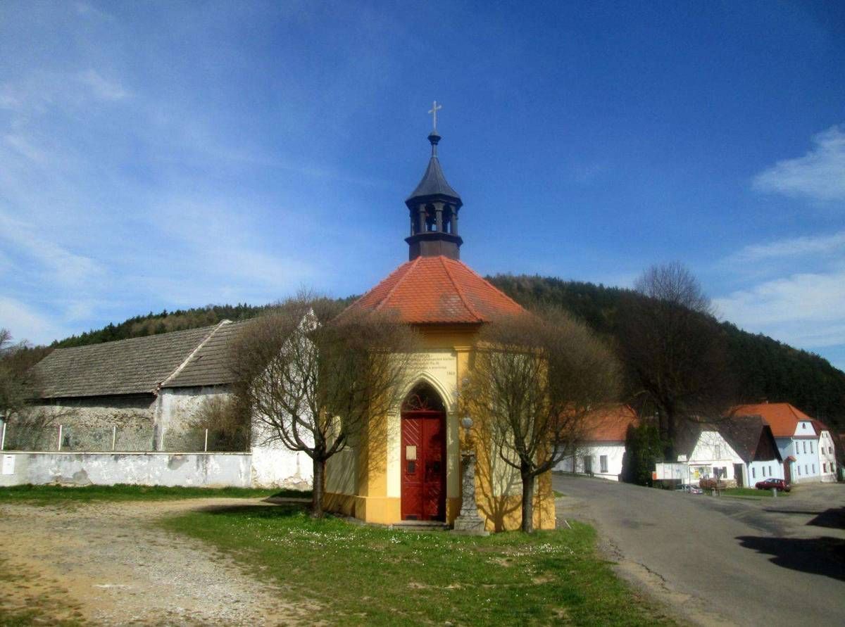 The image shows a small church with a red door in the middle of a small town, surrounded by houses...
