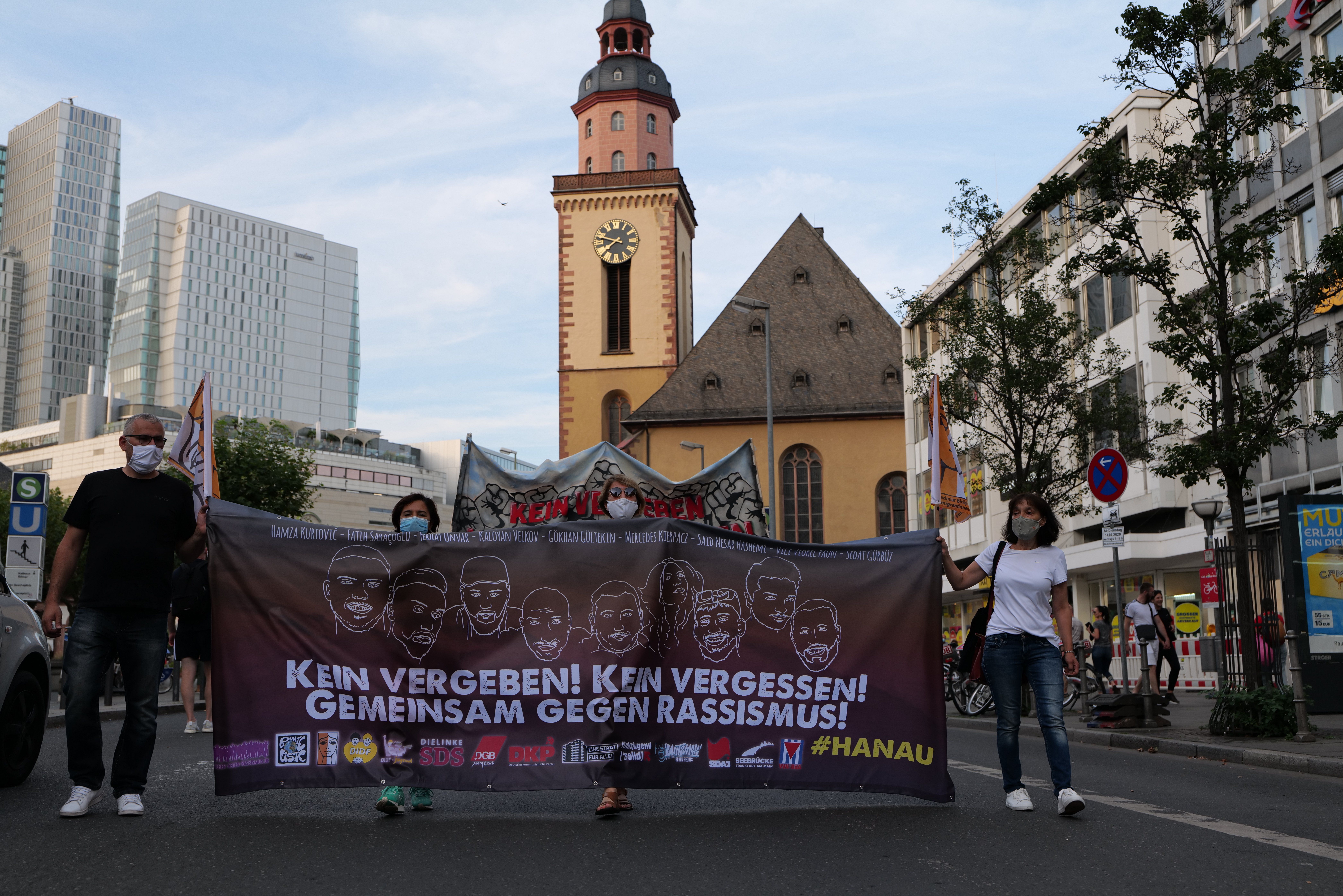 The image shows a group of people walking down a street, holding a banner with text and images on...