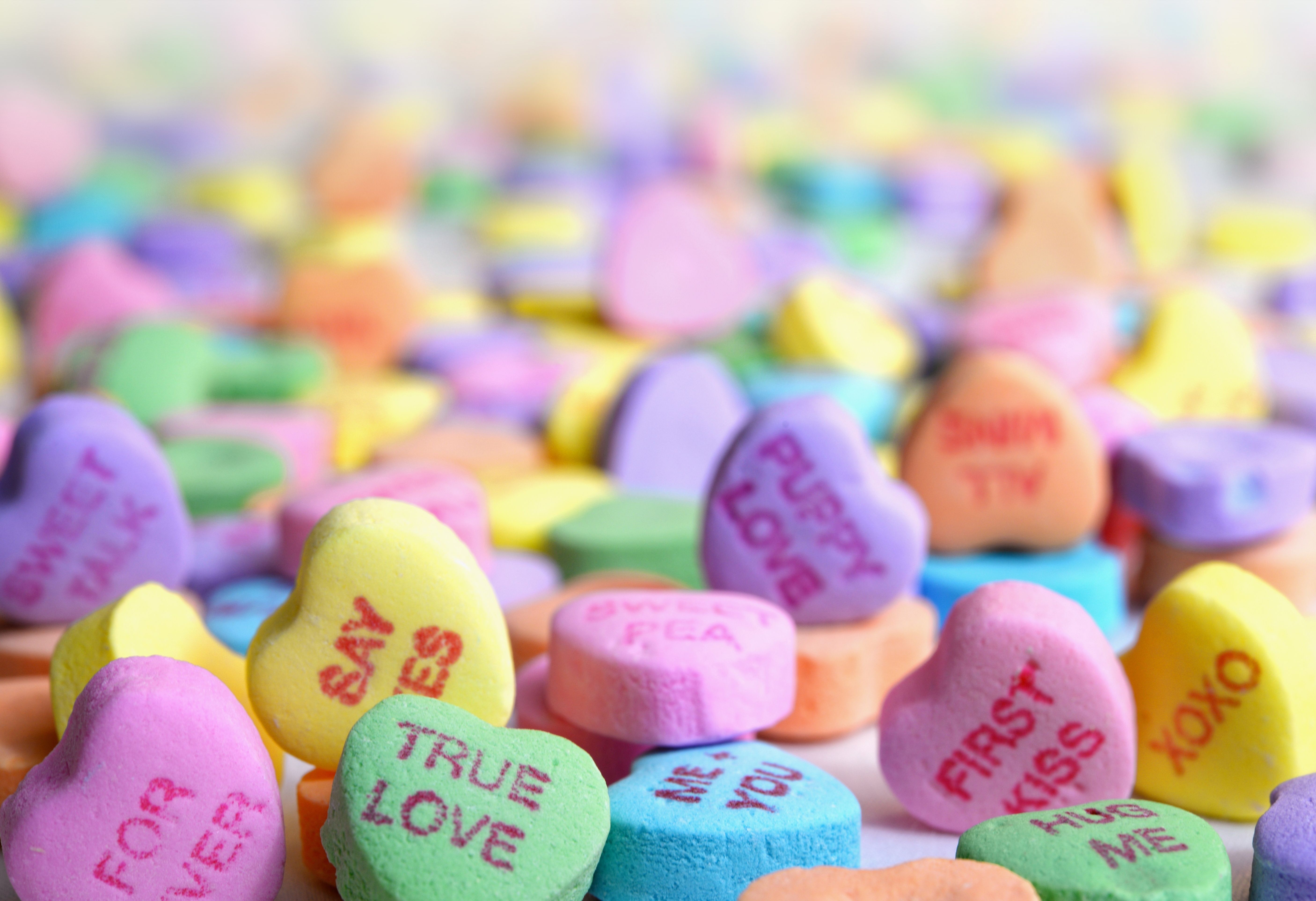The image shows a pile of colorful conversation hearts with the words "True Love" written on them,...
