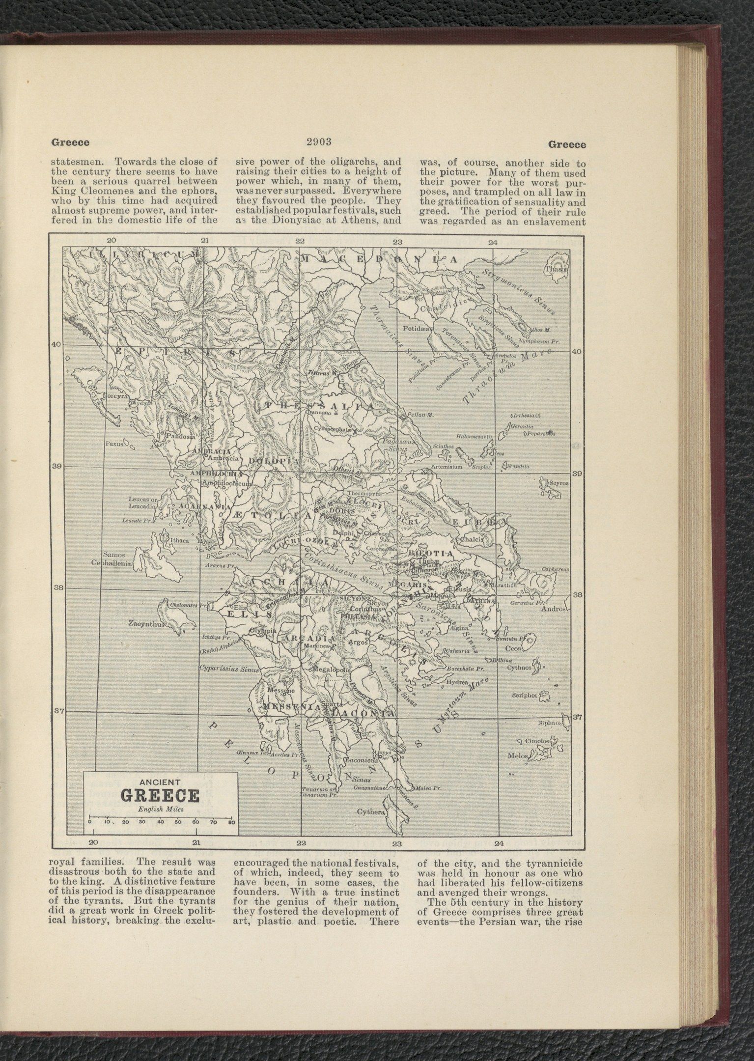The image shows an open book with a map of Greece on it, placed on a black surface. The book...