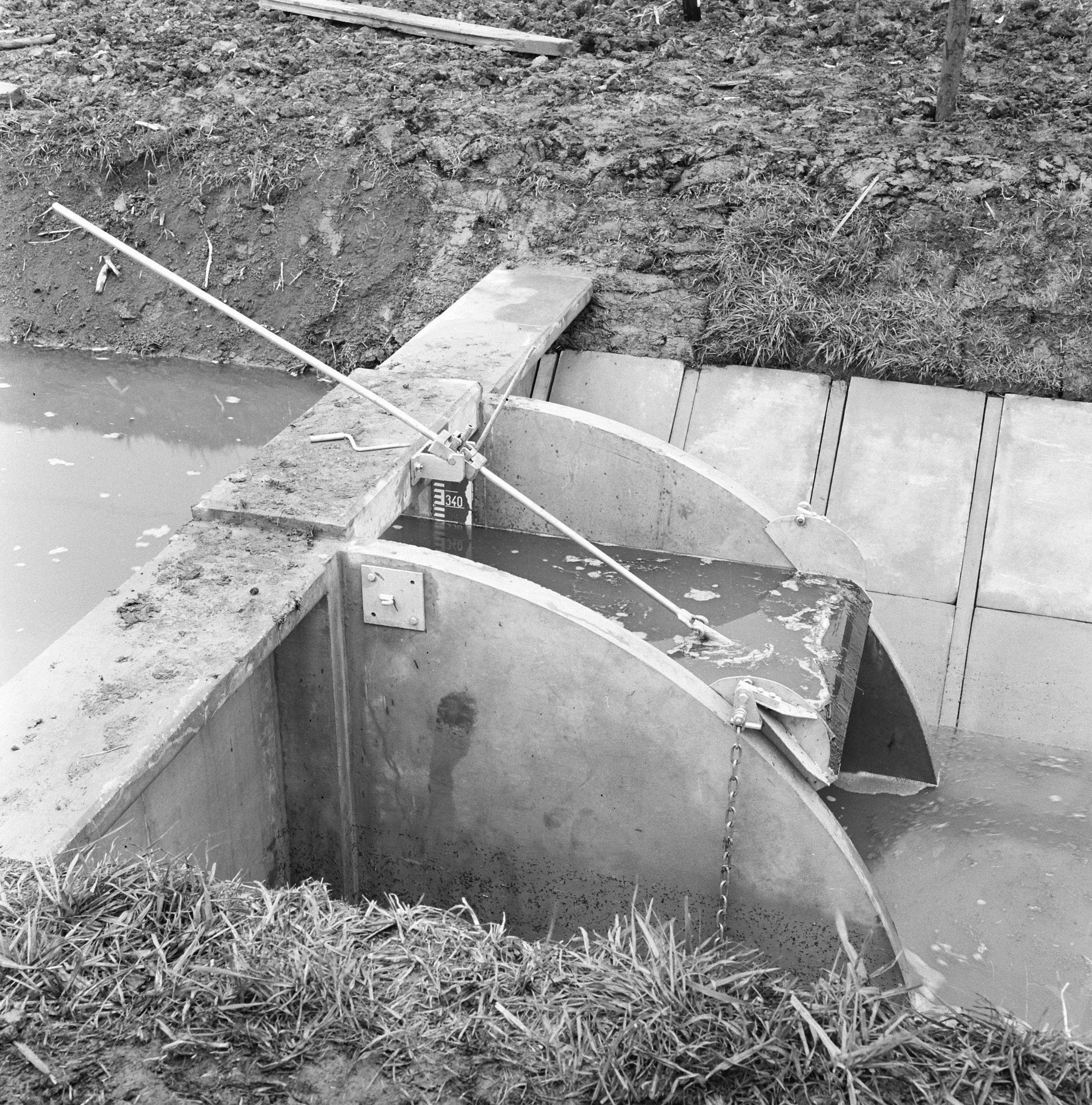 The image shows a black and white photo of a septic tank in the middle of a grassy area. The tank...