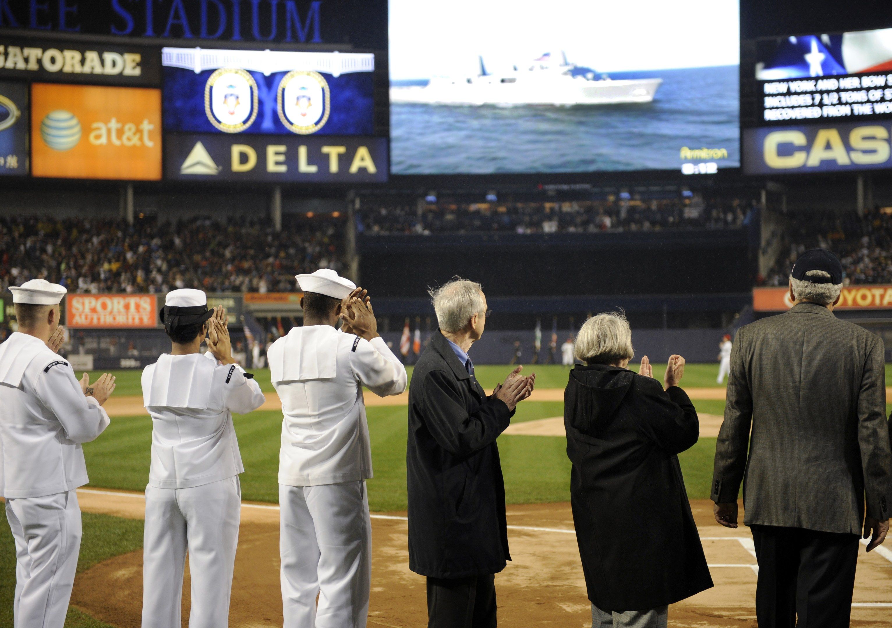 The image shows a group of people standing on top of a baseball field, clapping their hands in...