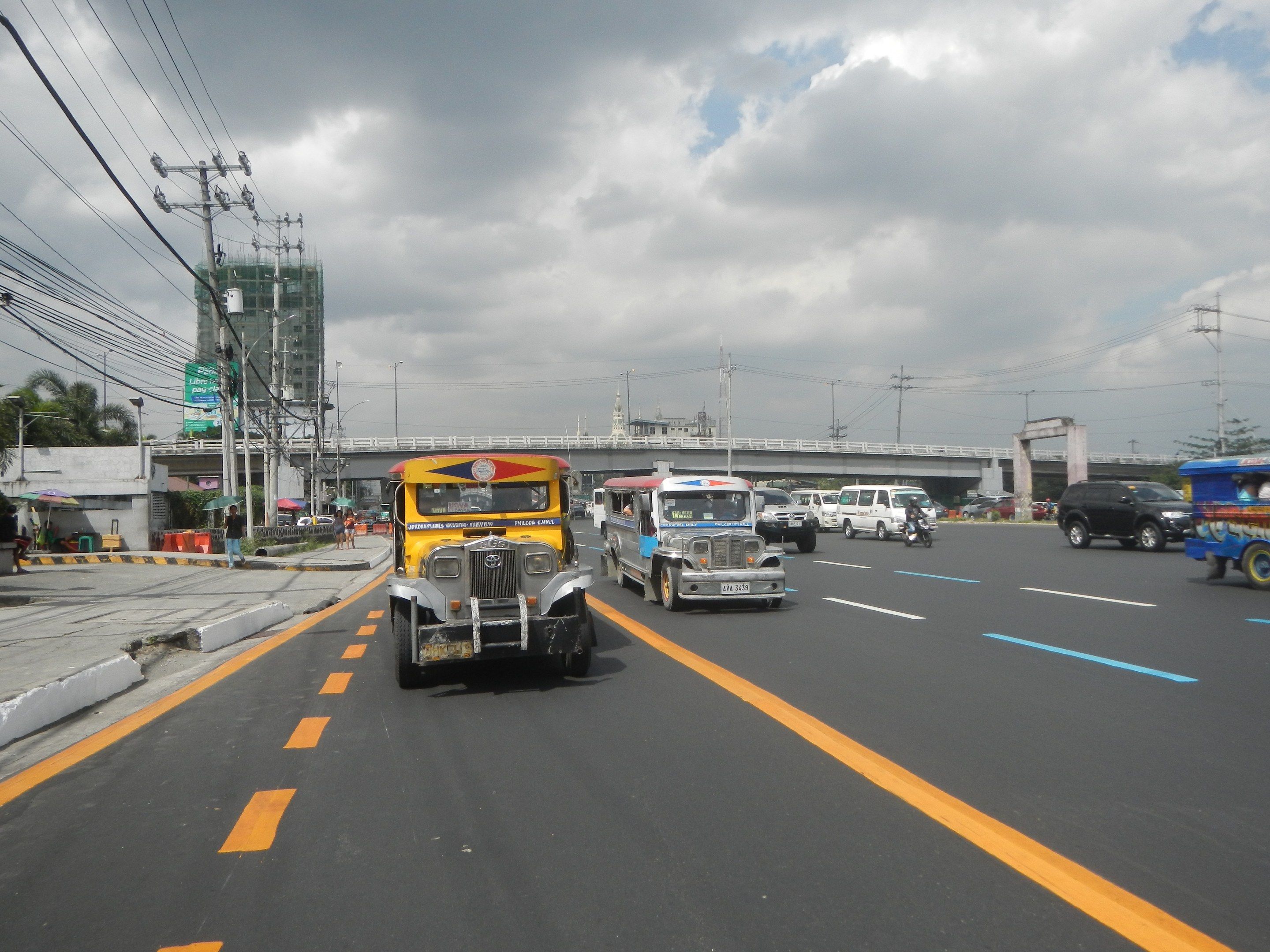 The image shows a busy street with a variety of vehicles, including a jeepney, driving down it. On...