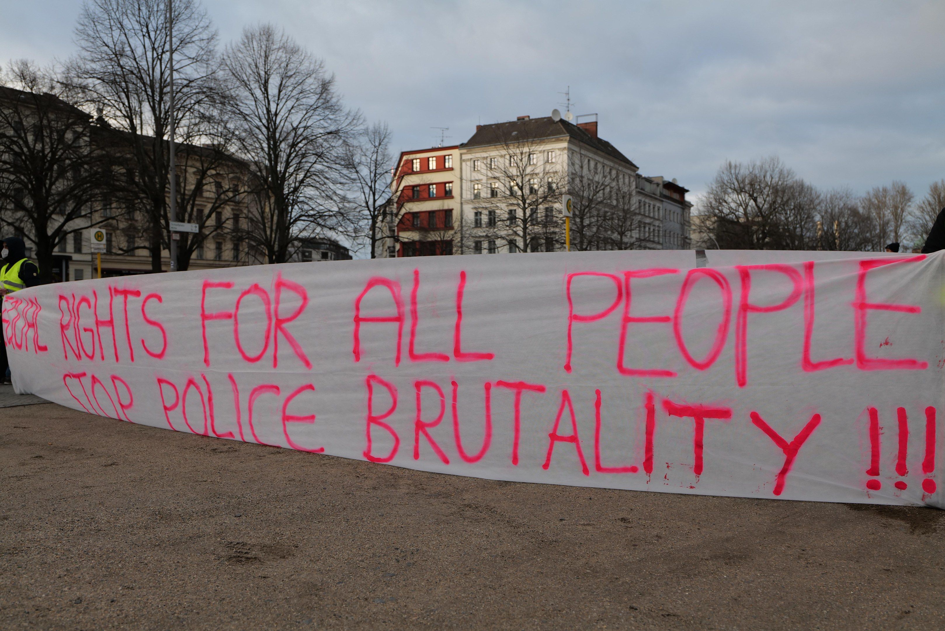The image shows a group of people standing on the ground, holding a banner that reads "Rights for...