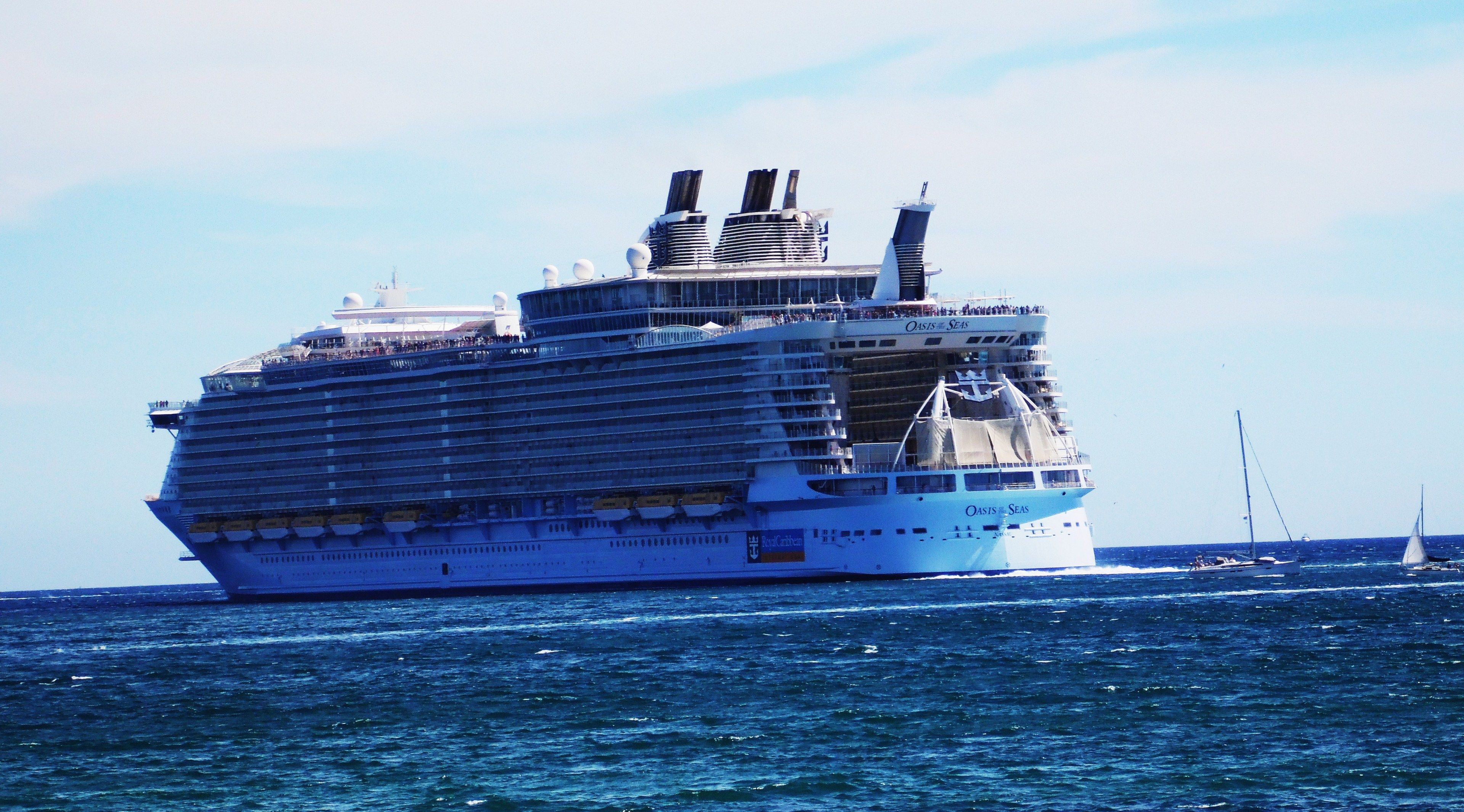 The image shows Royal Caribbean's Oasis of the Seas, a large cruise ship, sailing on the water with...