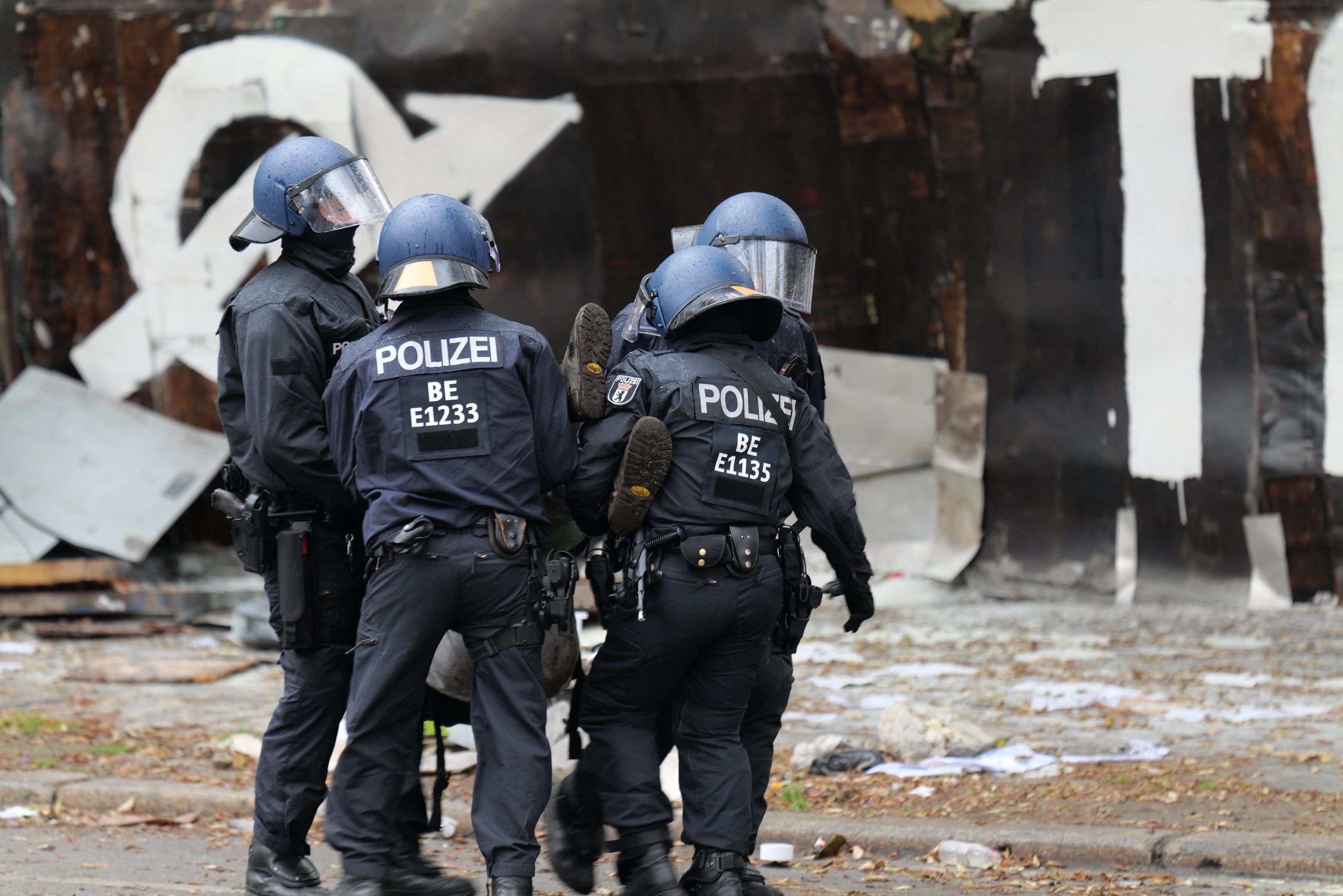 The image shows a group of police officers standing in front of a building with graffiti on it....
