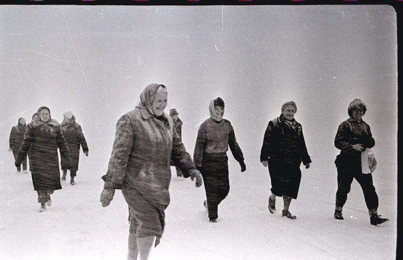 The image shows a group of people walking across a snow covered field, all wearing coats and caps....
