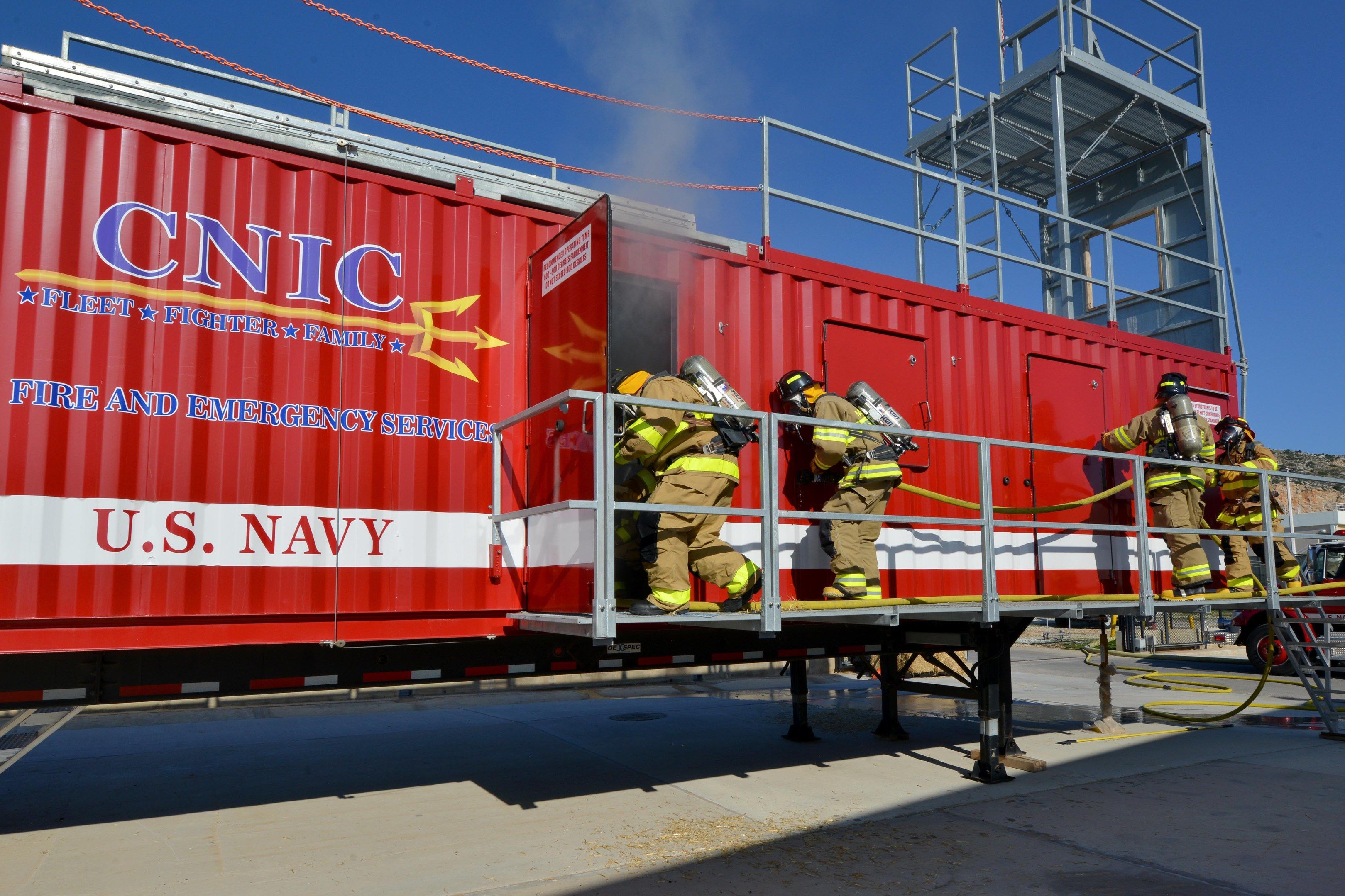 The image shows a group of firefighters wearing helmets and holding pipes, standing on top of a red...