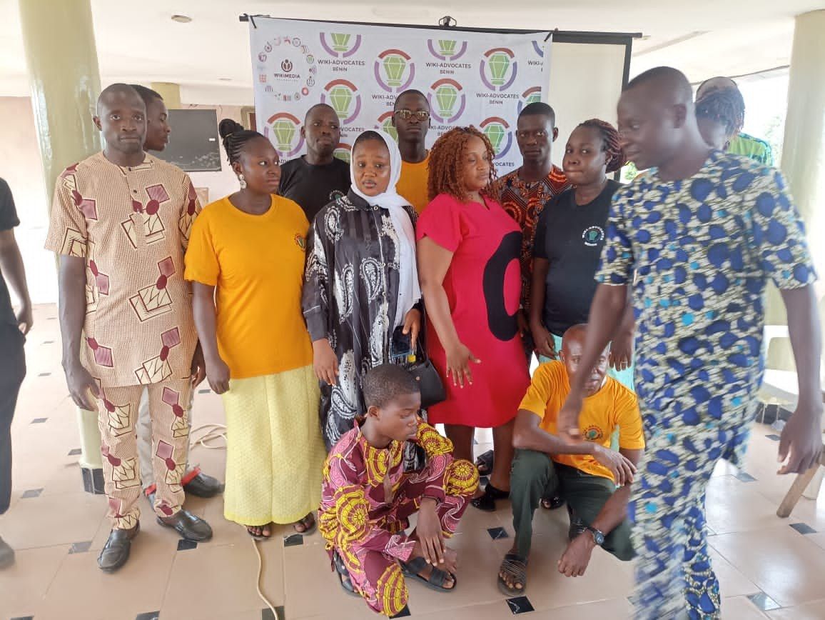 The image shows a group of people standing in front of a banner with text on it, surrounded by...