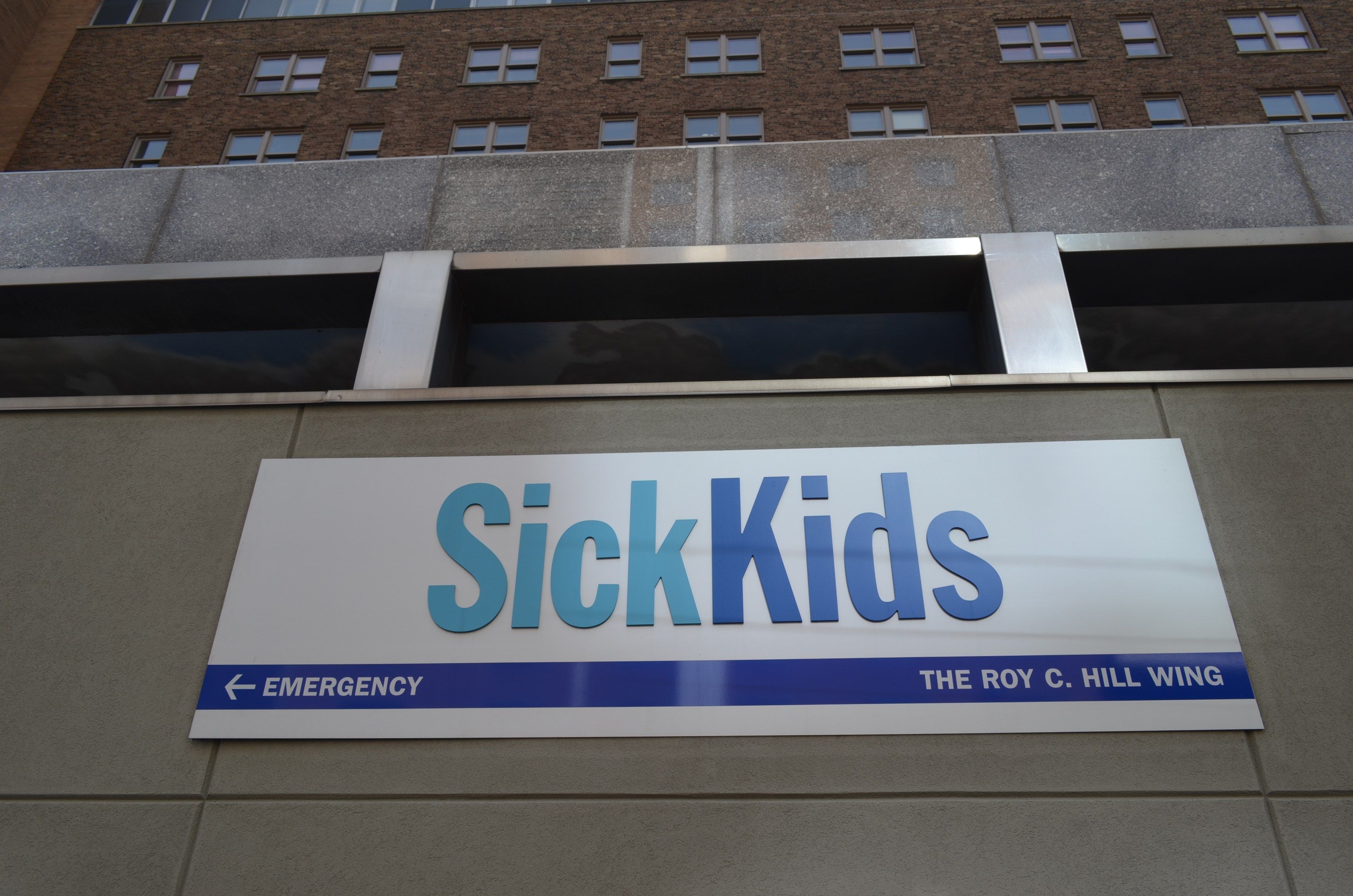 The image shows a building with a sign that reads "Sick Kids" on the side of it. The building has...