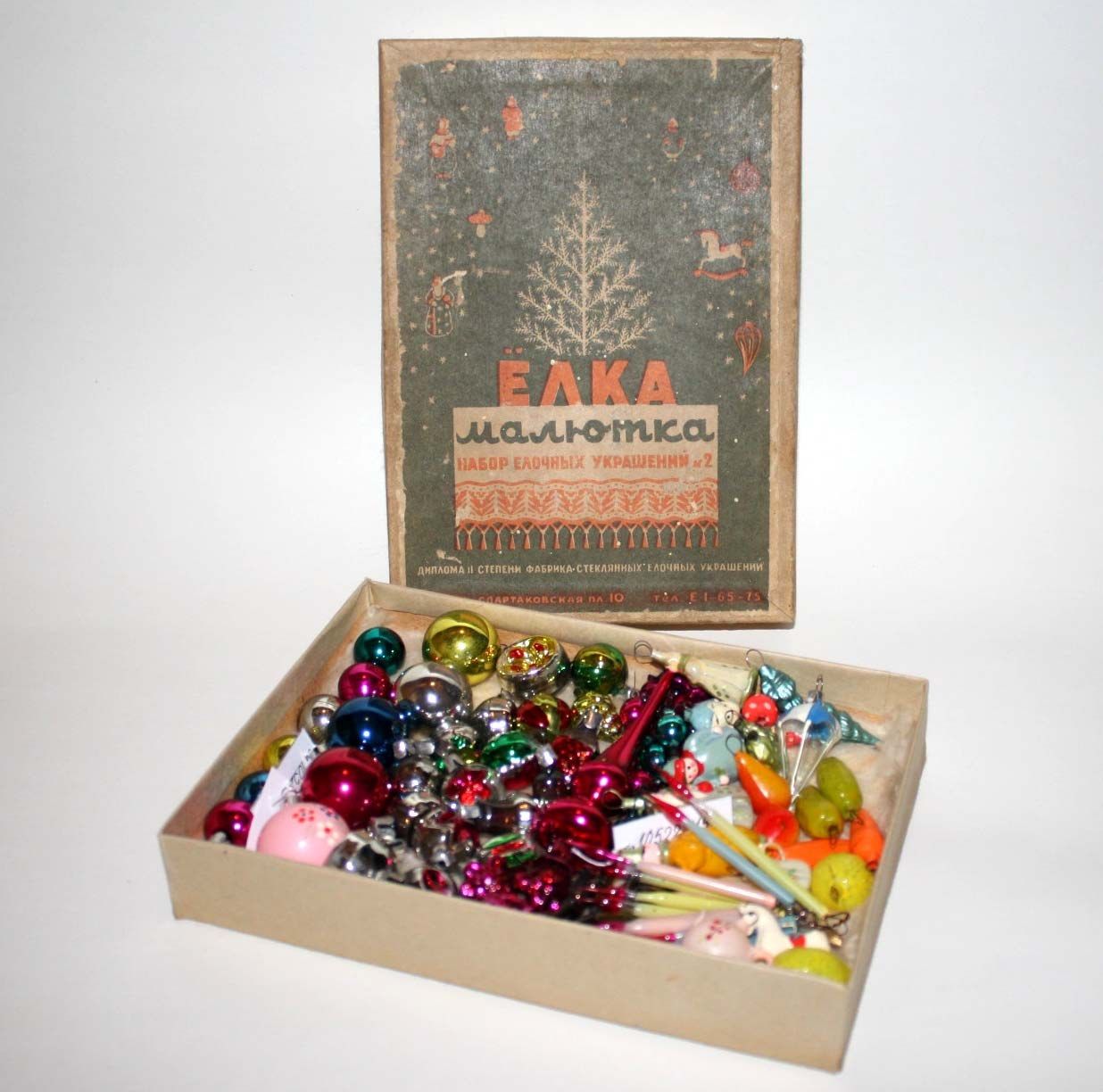 The image shows a box filled with lots of colorful Christmas ornaments sitting on top of a table....