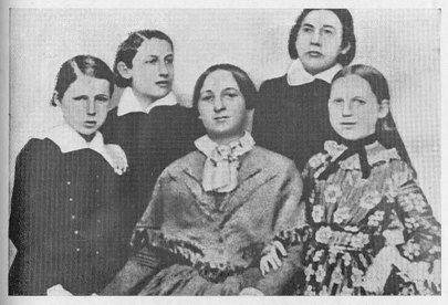 The image shows a black and white photo of a group of women, with one of them sitting in the...