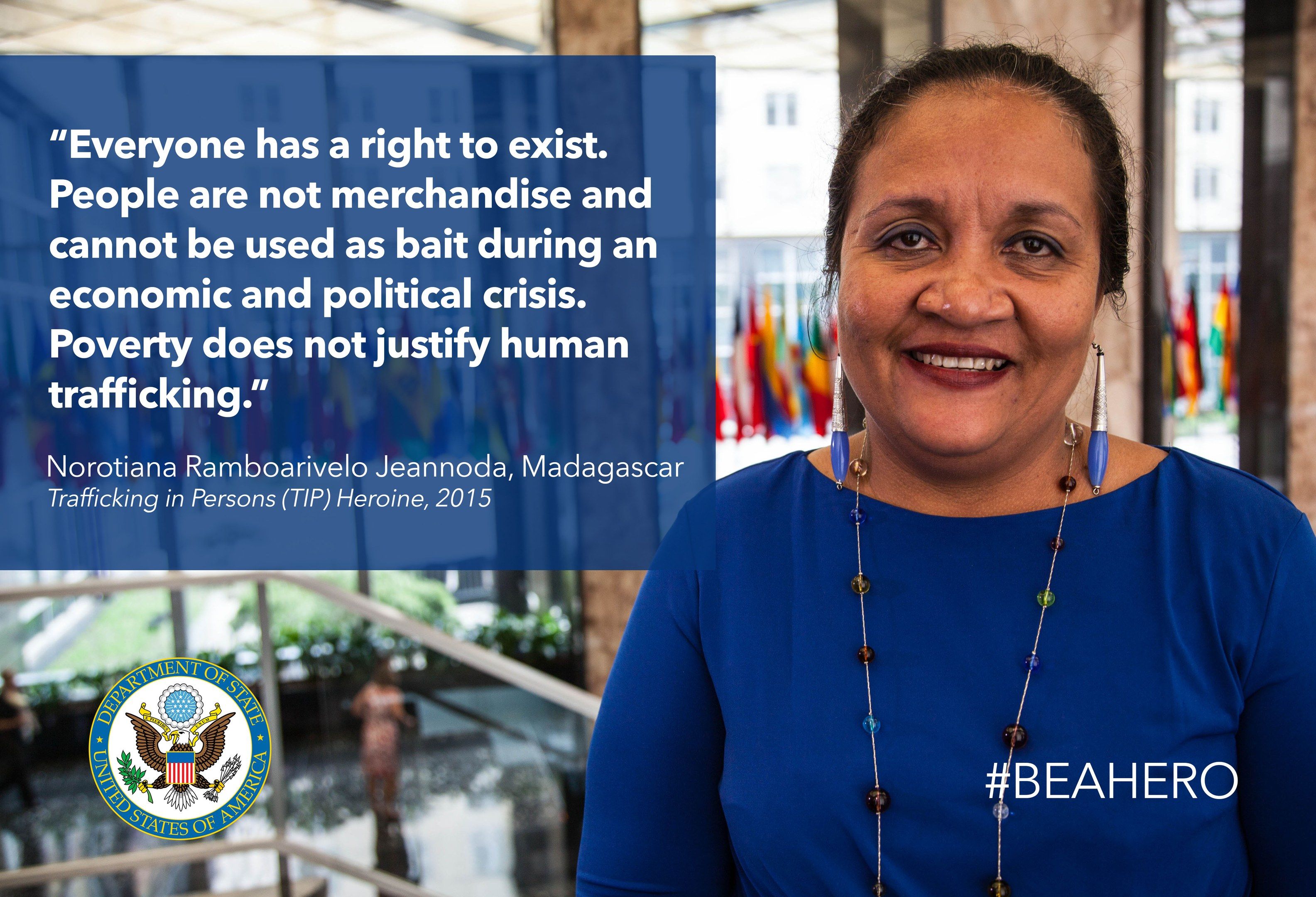 The image shows a woman in a blue dress standing in front of a building with a quote on it that...