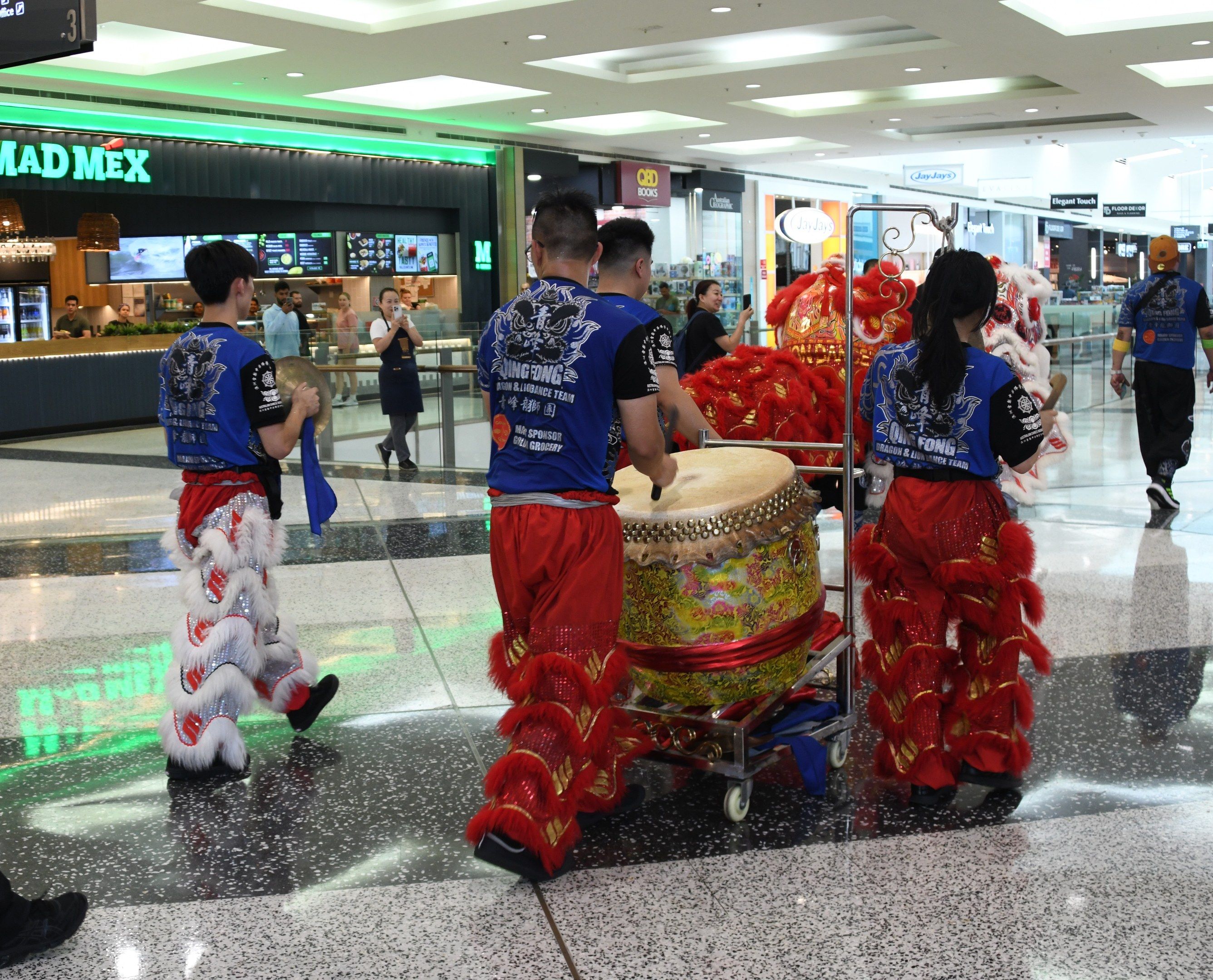 The image shows a group of people in red and blue outfits walking through an airport, with some of...