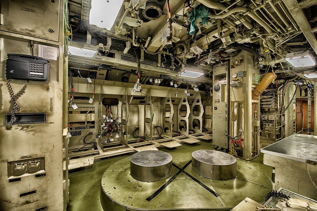The image shows the inside of a submarine with a lot of equipment, including two round tables on...