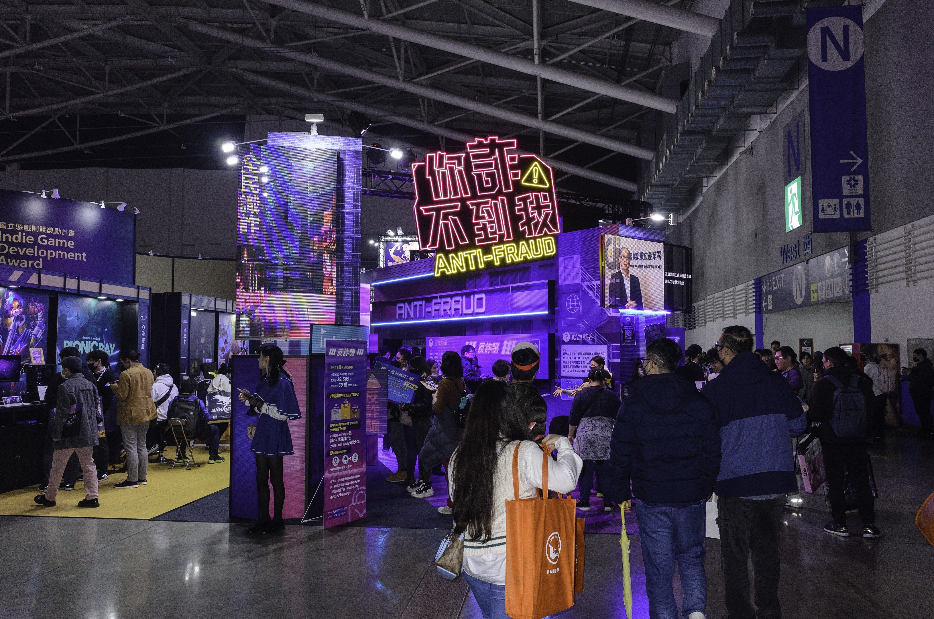 The image shows a large group of people standing in front of a booth at a trade show, with some of...