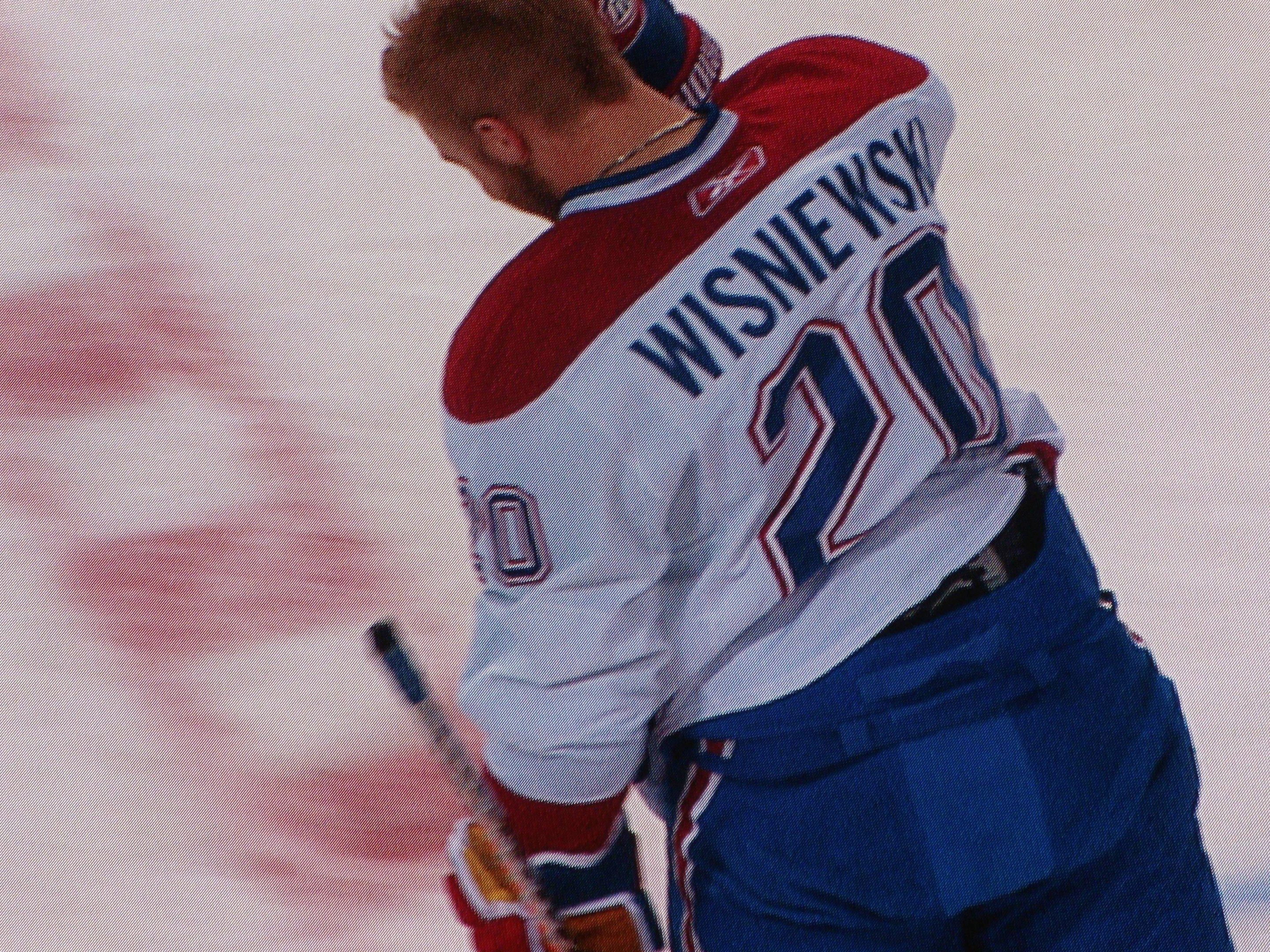 The image shows a hockey player standing on the ice, holding a hockey stick in his hand. He is...